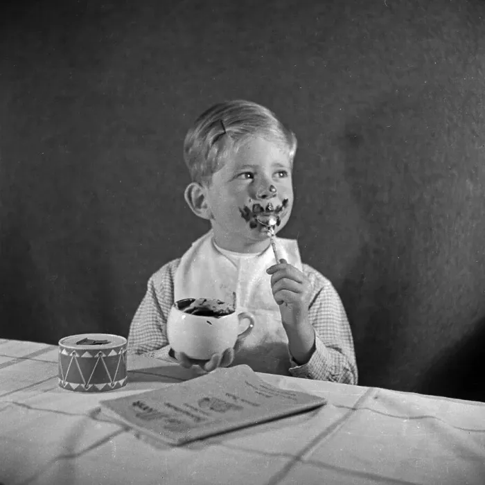 Impresión enmarcada : Kinder. Un pequeño niño come una taza de pudín de chocolate y se vuelve Impresión enmarcada : Kinder. Un pequeño niño come una taza de pudín de chocolate y se vuelve