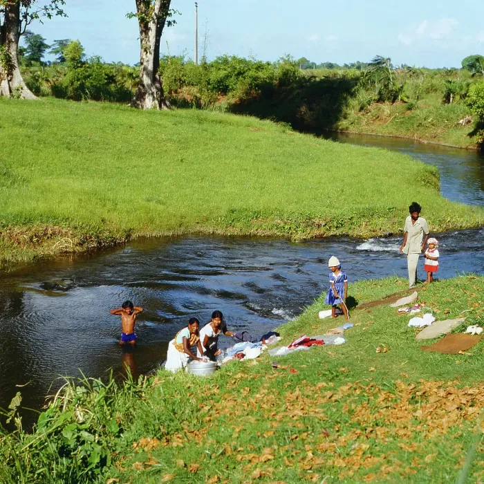 Gerahmter Druck : Mauritius. Frauen bei der Waschung ihrer Kleidung am Fluss in Mauritius, 1984 Gerahmter Druck : Mauritius. Frauen bei der Waschung ihrer Kleidung am Fluss in Mauritius, 1984